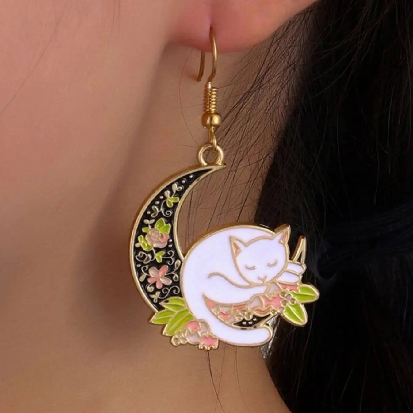 Cat moon dangle and drop earrings featuring a white cat sleeping on a decorated crescent moon with floral accents in pink, gold, and green.